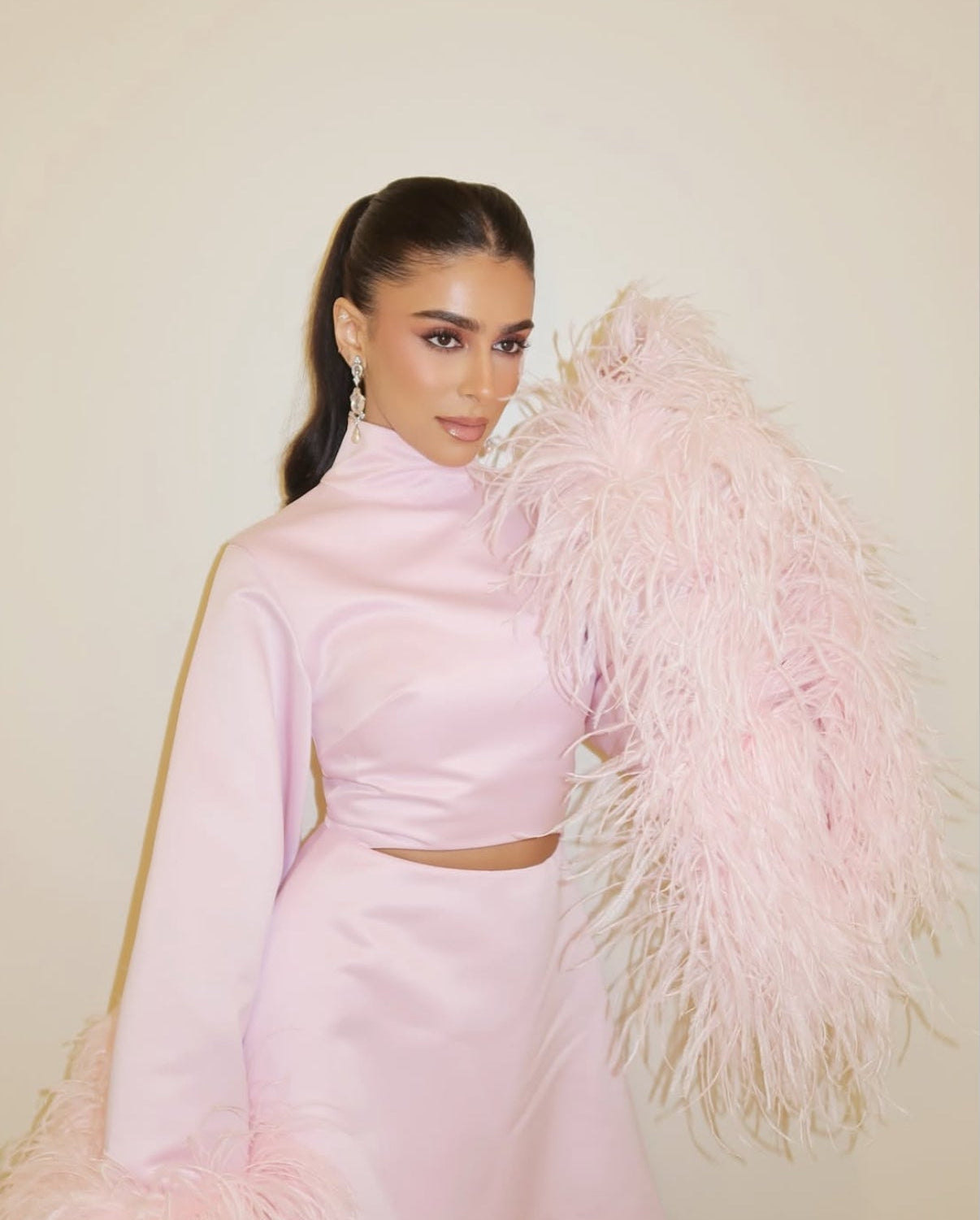 Woman in a pink outfit with feathered accessory against a neutral background

